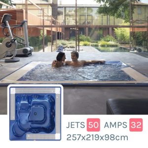 Two people relaxing in an indoor rectangular spa tub; inset shows a blue jet module with dimensions 257×219×98 cm and jet ratings (50 amps, 32).