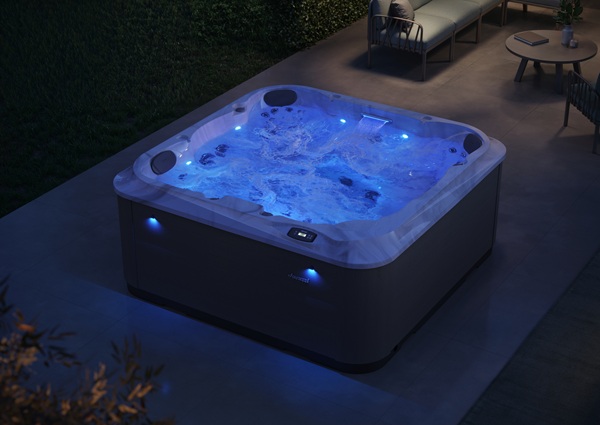 Outdoor rectangular hot tub bubbling with blue LED lights on a concrete patio at dusk, with seating nearby.