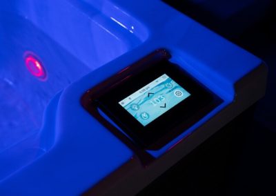 Touchscreen control panel mounted on the edge of a blue-lit hot tub, displaying settings on its screen