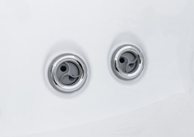 Two round spa jet outlets embedded in a white bathtub surface, seen from above.