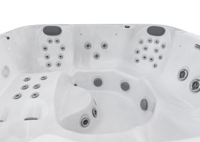 White acrylic hot tub with multiple seating areas and numerous jet nozzles, including built-in headrests.
