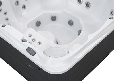 White acrylic hot tub interior with multiple jet nozzles and built-in seating, edge-mounted control panel visible on dark exterior.