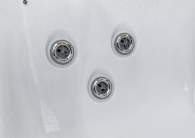 Close-up of three circular hot tub jets embedded in a white glossy tub surface.