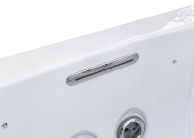 Close-up of a white bathtub side panel showing a horizontal silver vent/slot and a circular chrome control knob.