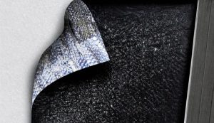 Close-up of a curled corner peeling away from a dark, rough textured surface, revealing white wall beneath with a metal edge on the right.