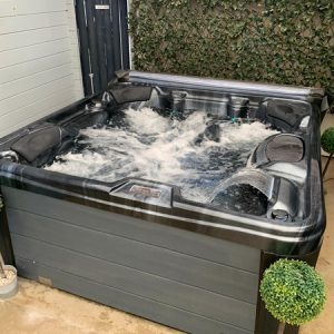 Outdoor hot tub with bubbling jets in a backyard courtyard, flanked by two potted topiary balls.