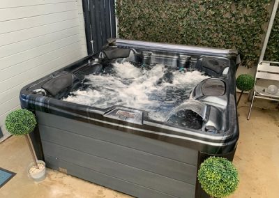 Outdoor hot tub with bubbling jets in a backyard courtyard, flanked by two potted topiary balls.