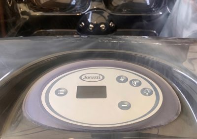 Jacuzzi hot tub control panel with a small digital display and round function buttons under a protective lid