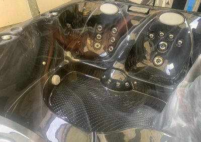 Two-person black hot tub interior with multiple jet nozzles built into each seat, a textured footwell, and white headrests at the top.