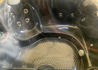 Interior of a black hot tub with multiple jet nozzles and a textured floor surface.