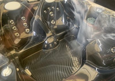 A black spa foot massage chair with multiple jet nozzles and a textured foot basin, covered in a clear plastic wrap.