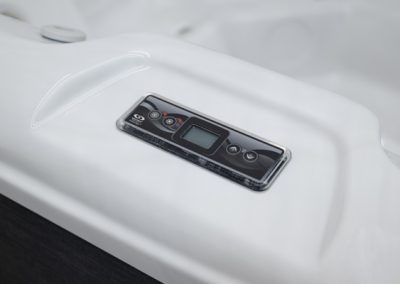 Close-up of a digital control panel embedded in a white hot tub, featuring a small display and round buttons.