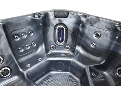 Interior of a stainless steel hot tub with numerous jets and a central water inlet panelhead, gleaming metallic finish.
