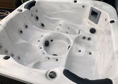 White hot tub interior with multiple jets and built-in seating, plus a side control panel.